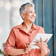 Woman smiling while looking out window and holding tablet