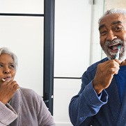 Couple smiling while brushing their teeth in bathroom