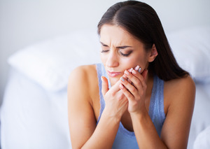 Woman sitting on bed with facial pain